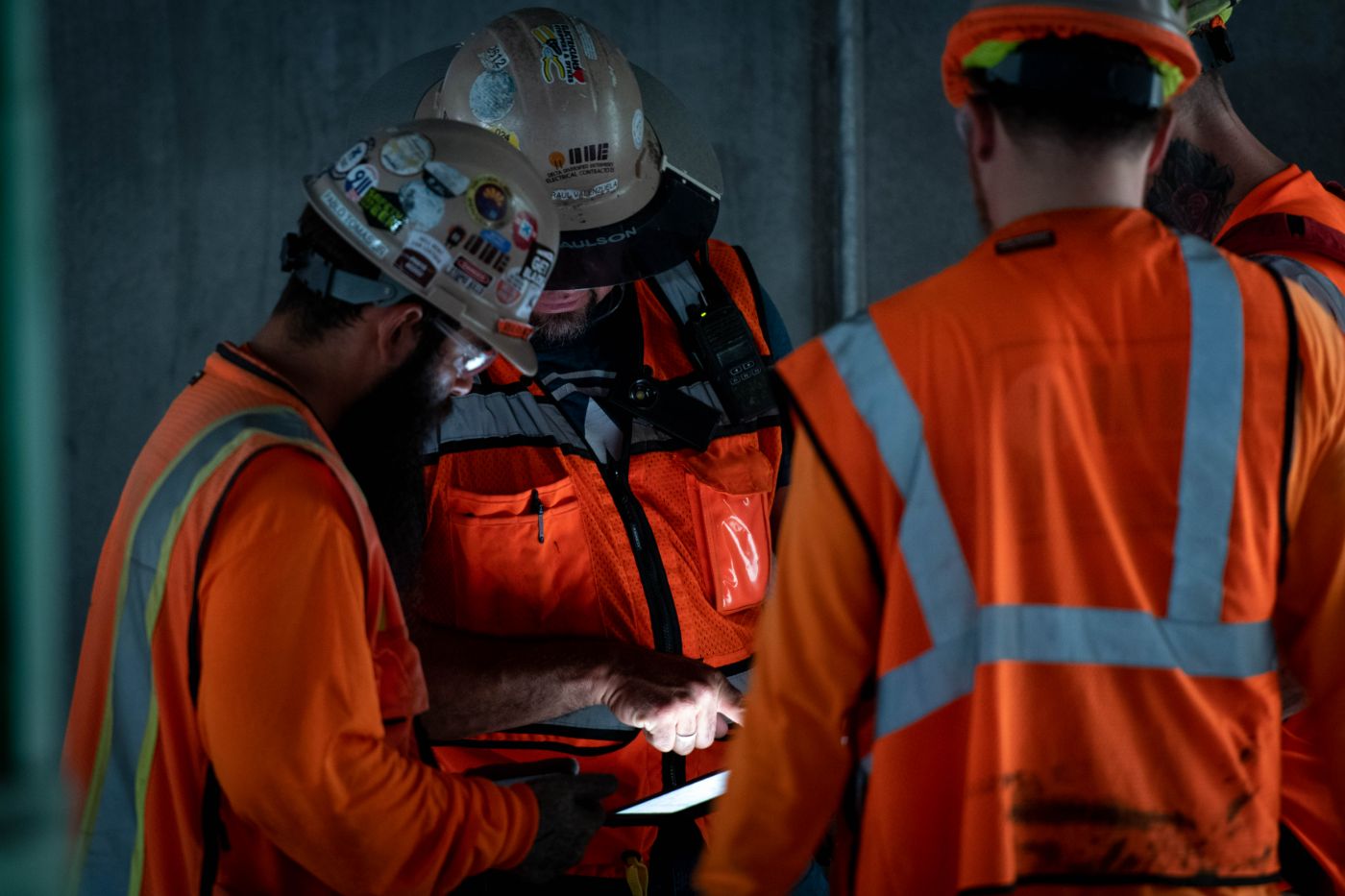 Trade crew in orange vests reviewing drawings on a phone